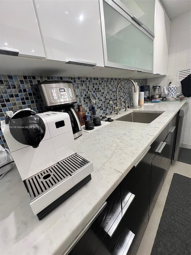 kitchen featuring light stone counters, backsplash, a sink, and glass insert cabinets