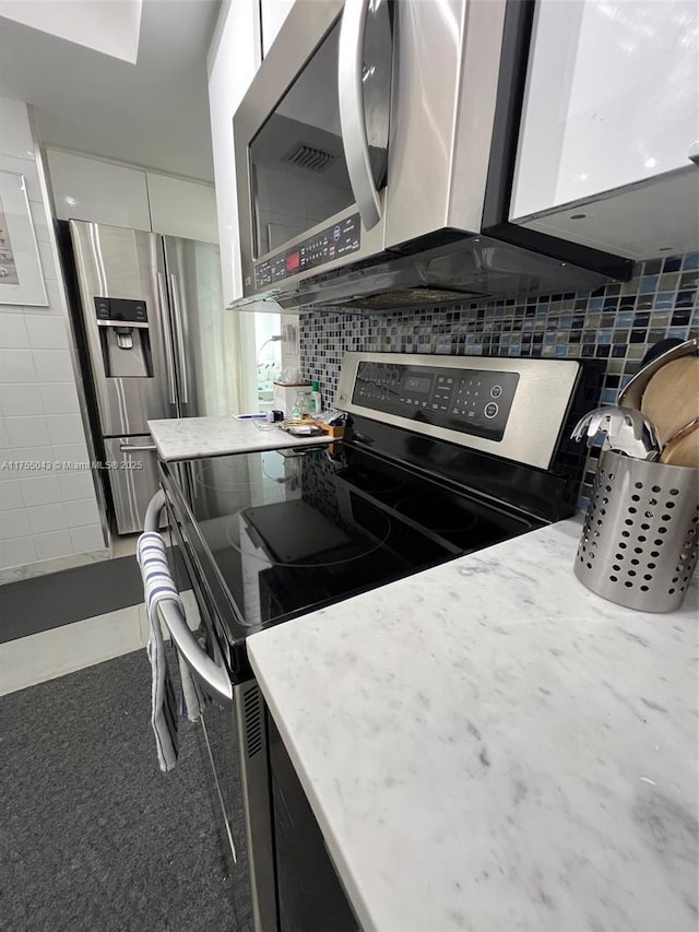 kitchen with stainless steel appliances, light stone counters, tile walls, and decorative backsplash