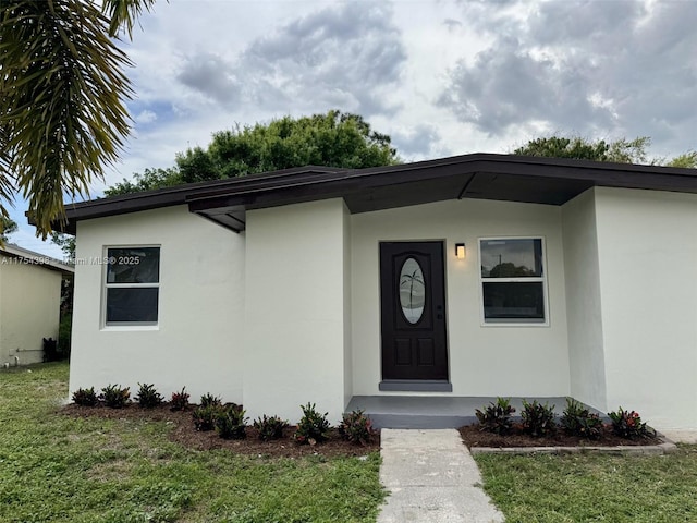 view of exterior entry with stucco siding and a yard