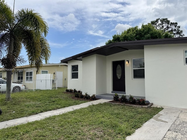 ranch-style house with a front yard, fence, and stucco siding