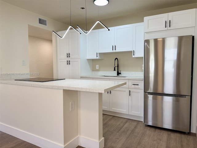 kitchen featuring visible vents, wood finished floors, freestanding refrigerator, white cabinetry, and a sink