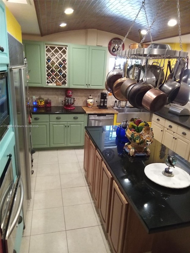 kitchen featuring tasteful backsplash, stainless steel appliances, vaulted ceiling, green cabinets, and light tile patterned flooring