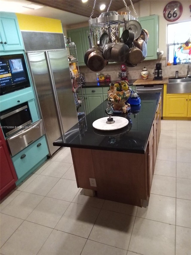 kitchen with light tile patterned floors, tasteful backsplash, dark countertops, a kitchen island, and a sink