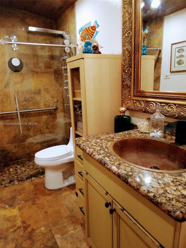 bathroom with stone finish floor, a tile shower, vanity, and toilet