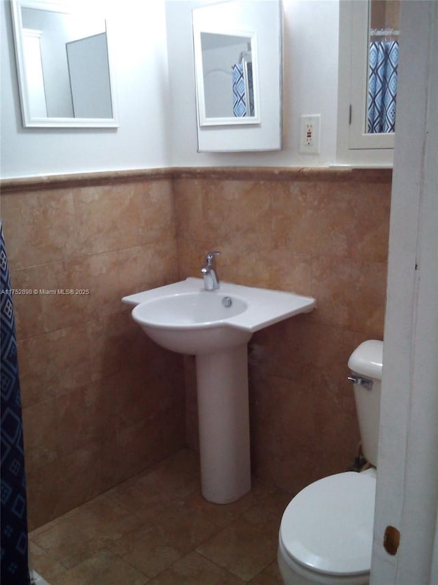 bathroom featuring a wainscoted wall, tile patterned flooring, toilet, and tile walls