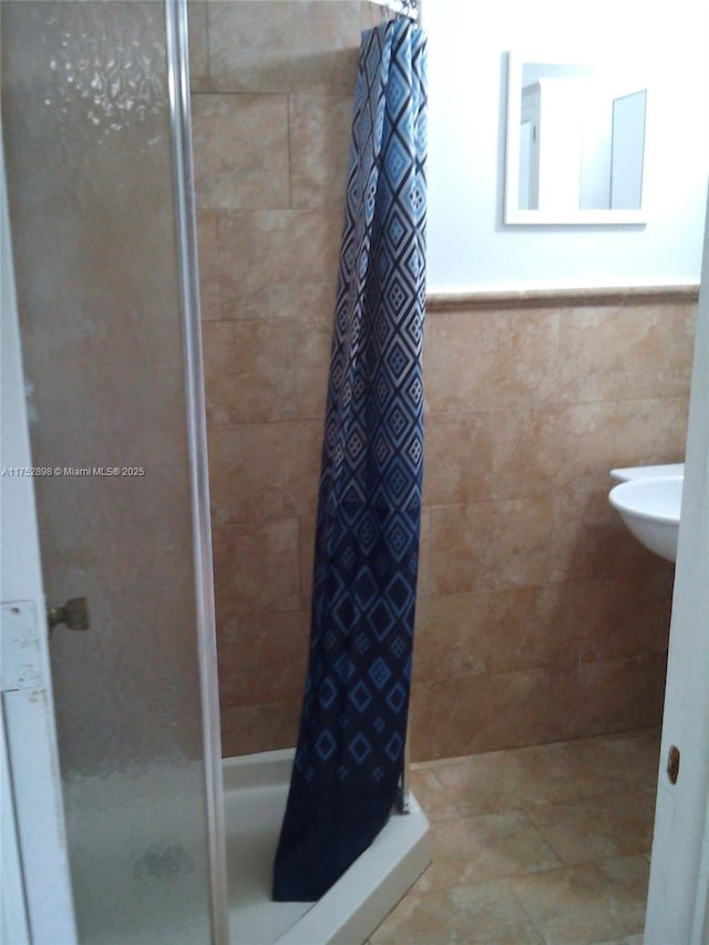 bathroom with a wainscoted wall, a shower stall, and tile walls