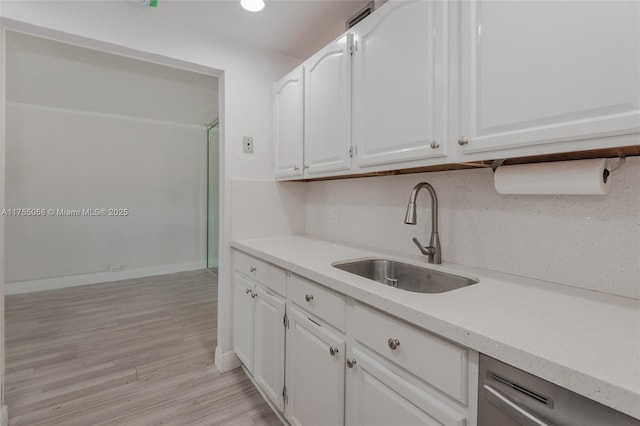 kitchen featuring white cabinets, dishwasher, light wood-style flooring, light countertops, and a sink