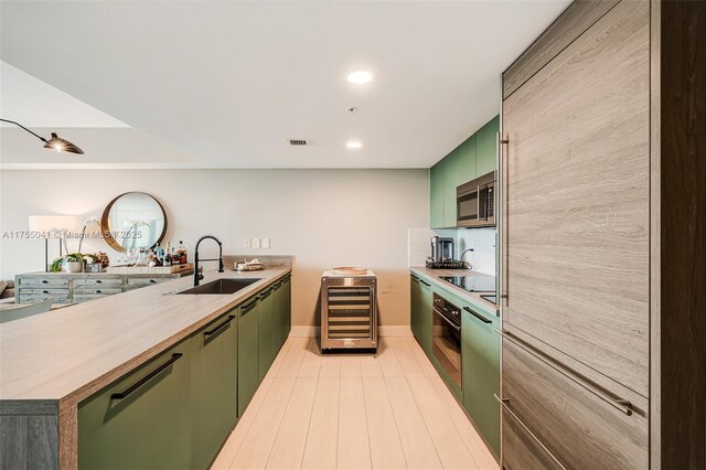 kitchen with wine cooler, a sink, green cabinetry, a peninsula, and black appliances