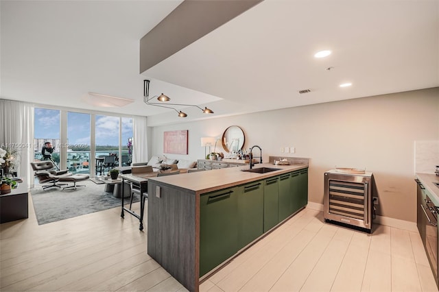 kitchen featuring a sink, a wall of windows, beverage cooler, green cabinetry, and a peninsula