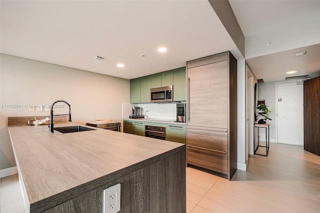 kitchen featuring stainless steel appliances, a peninsula, a sink, visible vents, and green cabinetry