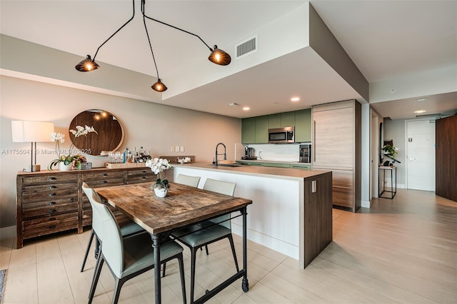 kitchen featuring a peninsula, a sink, visible vents, stainless steel microwave, and green cabinetry