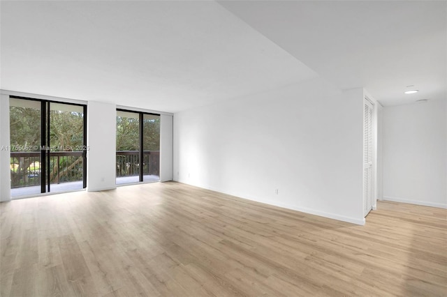 unfurnished room featuring floor to ceiling windows, light wood-style flooring, and baseboards