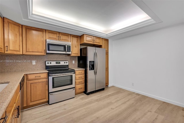 kitchen with light wood finished floors, appliances with stainless steel finishes, decorative backsplash, and a tray ceiling