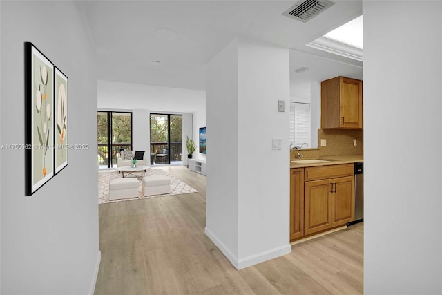 hallway with light wood finished floors, a sink, visible vents, and baseboards