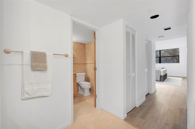 hall with baseboards, visible vents, light wood-style flooring, and tile walls