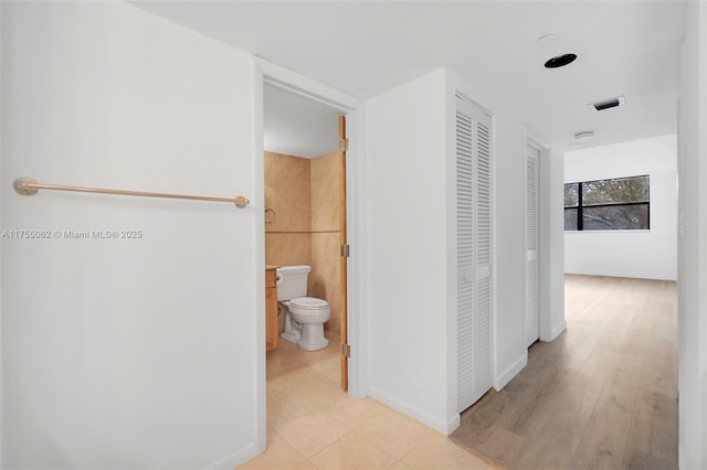 hall featuring visible vents, light wood finished floors, tile walls, and baseboards