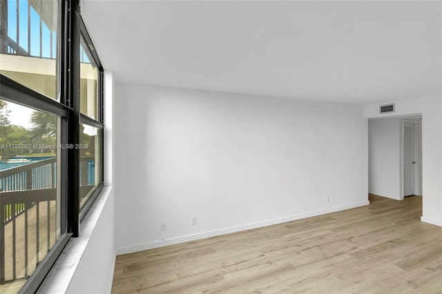 empty room featuring baseboards, floor to ceiling windows, visible vents, and light wood-style floors