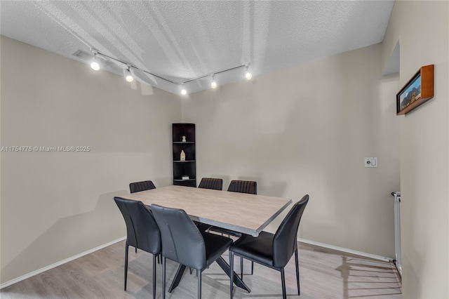 dining space featuring a textured ceiling, baseboards, and light wood-style floors