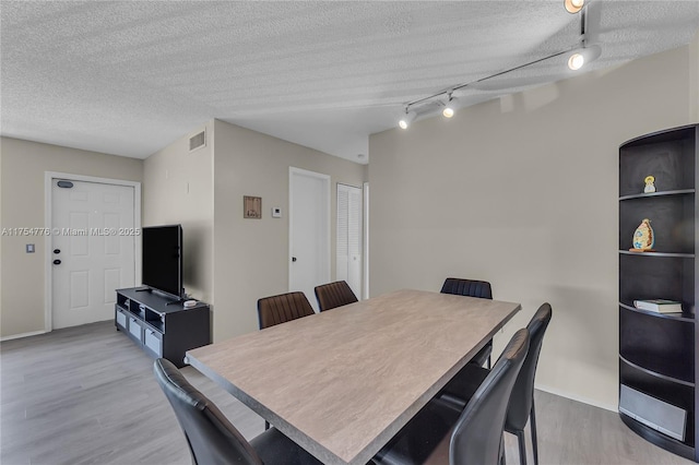 dining space featuring a textured ceiling, wood finished floors, visible vents, and track lighting