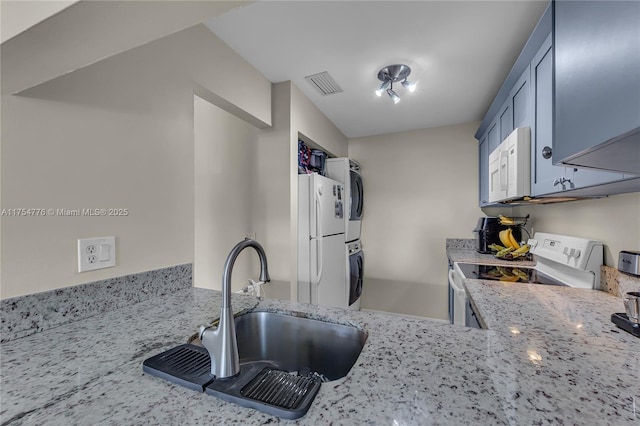 kitchen featuring light stone counters, white appliances, a sink, visible vents, and stacked washer and clothes dryer