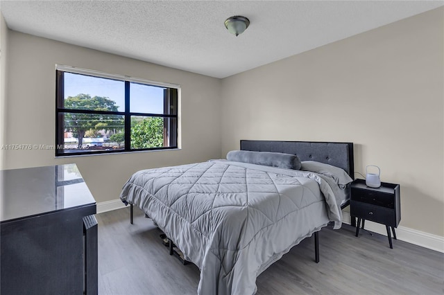 bedroom with a textured ceiling, baseboards, and wood finished floors