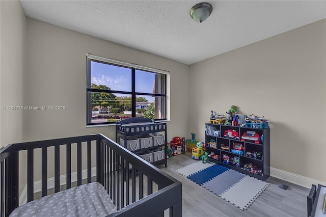 bedroom with a textured ceiling, baseboards, and wood finished floors