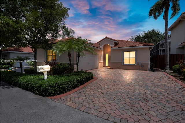 mediterranean / spanish-style house with a tile roof, an attached garage, fence, decorative driveway, and stucco siding