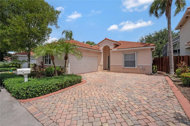 mediterranean / spanish-style house with decorative driveway, a tile roof, stucco siding, fence, and a garage