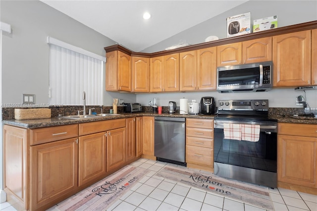 kitchen featuring light tile patterned floors, appliances with stainless steel finishes, vaulted ceiling, a sink, and dark stone counters