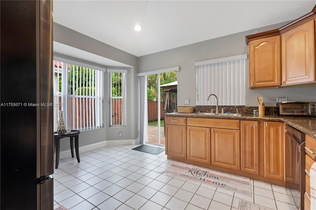 kitchen with light tile patterned flooring, a toaster, a sink, stainless steel dishwasher, and dark stone countertops