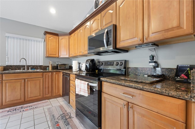 kitchen featuring appliances with stainless steel finishes, dark stone counters, a sink, and light tile patterned floors