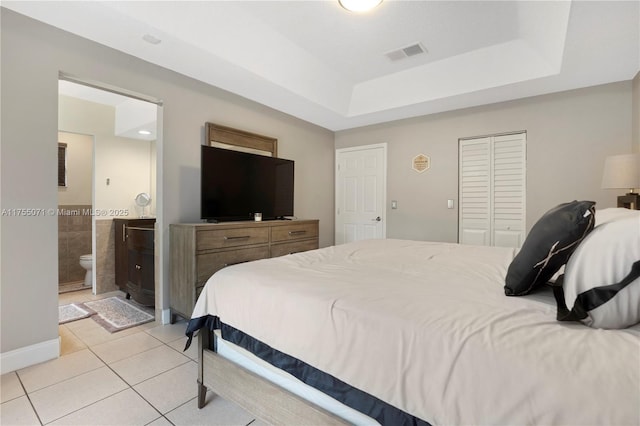 bedroom featuring ensuite bath, light tile patterned floors, visible vents, and a tray ceiling