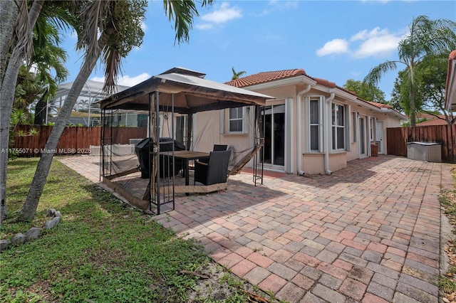 rear view of house featuring fence, a gazebo, a tiled roof, stucco siding, and a patio area