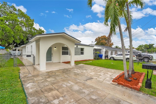 rear view of property featuring a lawn, a patio, a gate, fence, and stucco siding