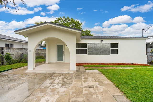 exterior space featuring a front lawn, a patio area, fence, and stucco siding