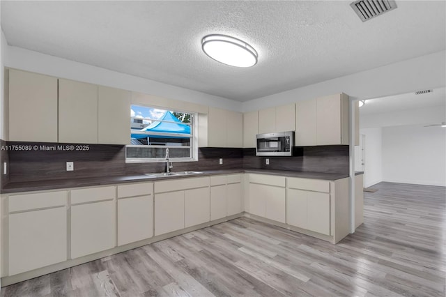 kitchen with a sink, visible vents, tasteful backsplash, stainless steel microwave, and dark countertops