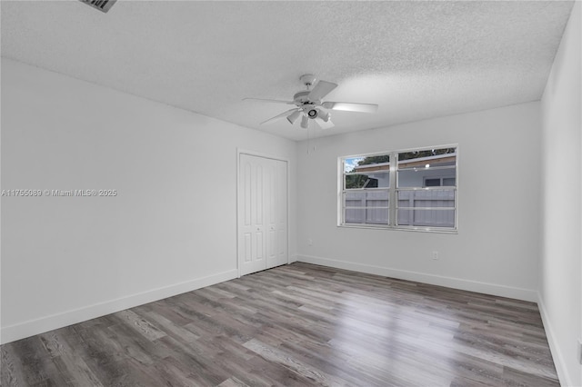 empty room with ceiling fan, a textured ceiling, wood finished floors, and baseboards