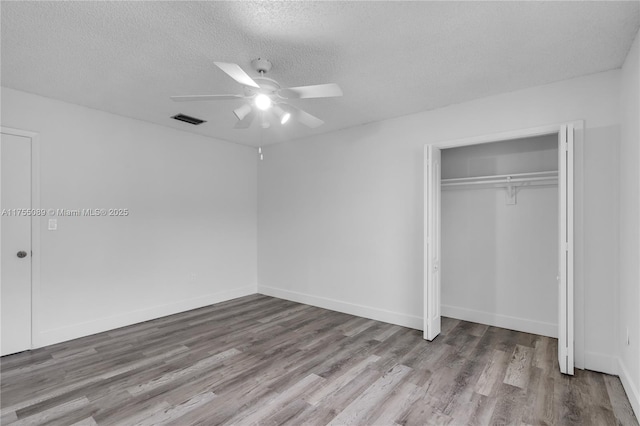 unfurnished bedroom featuring a textured ceiling, a closet, wood finished floors, and visible vents