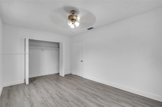 unfurnished bedroom featuring a closet, visible vents, a textured ceiling, wood finished floors, and baseboards