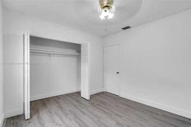 unfurnished bedroom with baseboards, visible vents, wood finished floors, a textured ceiling, and a closet