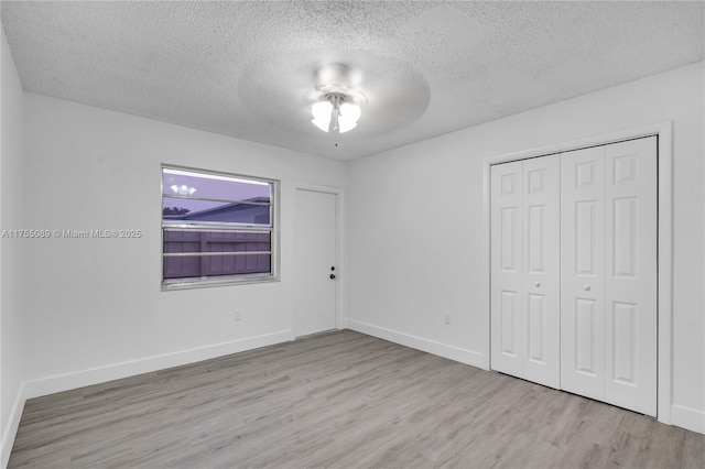 unfurnished bedroom featuring a closet, a textured ceiling, baseboards, and wood finished floors