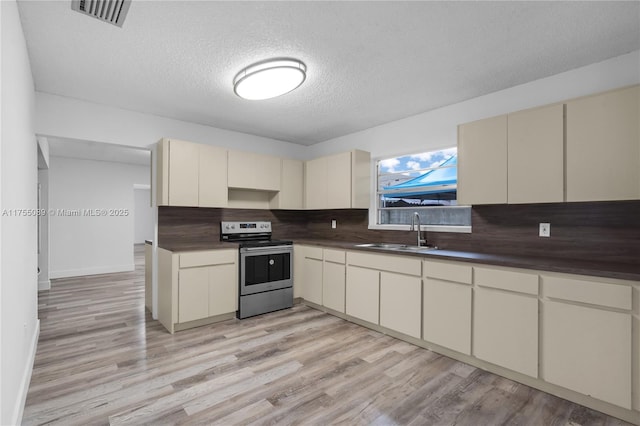 kitchen featuring electric stove, cream cabinets, dark countertops, and a sink