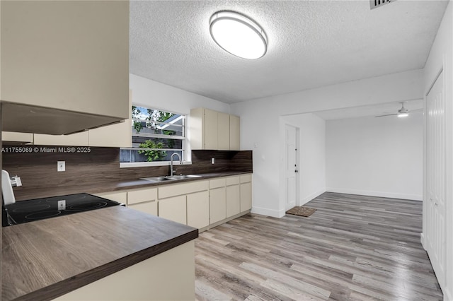 kitchen featuring range with electric cooktop, dark countertops, a sink, light wood-style floors, and backsplash