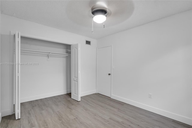 unfurnished bedroom with baseboards, visible vents, wood finished floors, a textured ceiling, and a closet