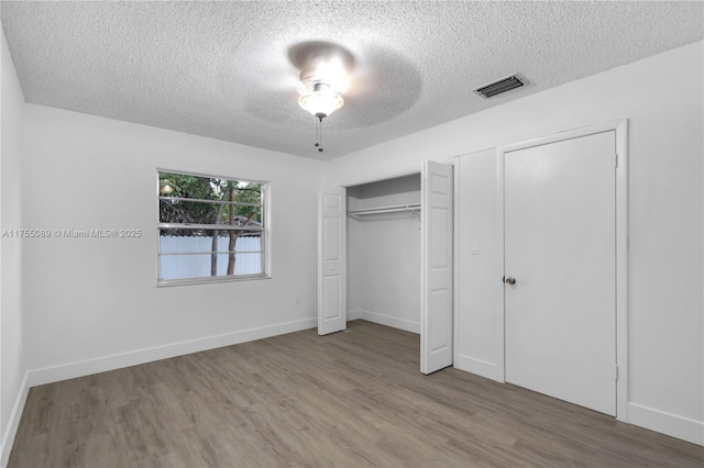 unfurnished bedroom featuring baseboards, a textured ceiling, visible vents, and wood finished floors