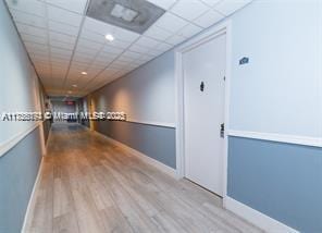 hallway with a paneled ceiling, baseboards, and wood finished floors