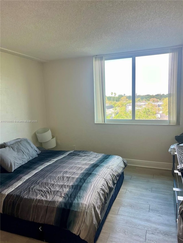 bedroom featuring baseboards, light wood finished floors, and a textured ceiling