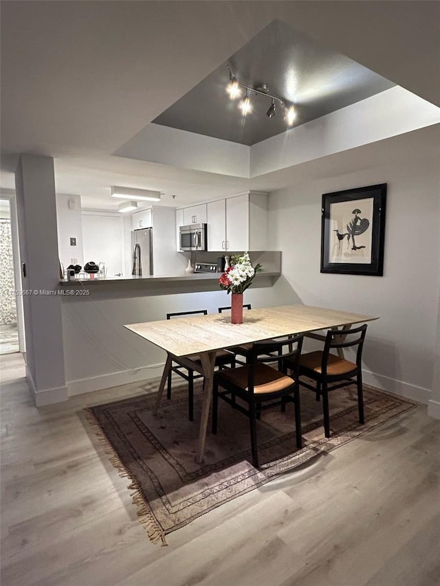 dining area featuring light wood-style floors, baseboards, and a tray ceiling