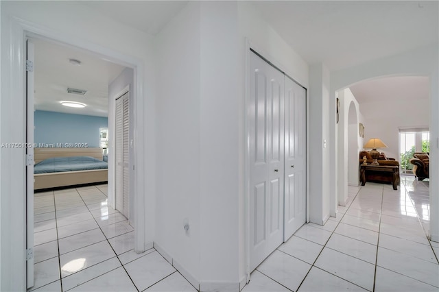 corridor with light tile patterned floors, visible vents, arched walkways, and baseboards