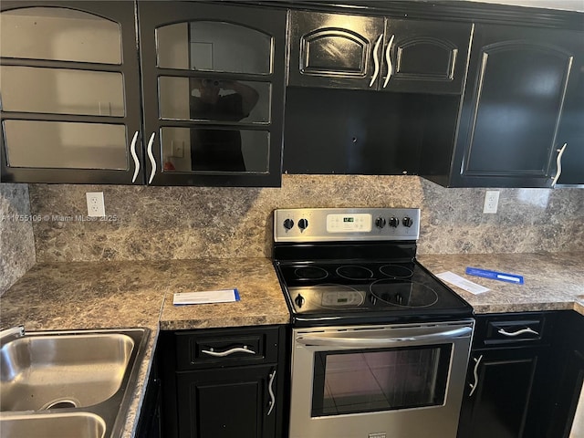 kitchen with a sink, stainless steel electric range, backsplash, and dark cabinetry